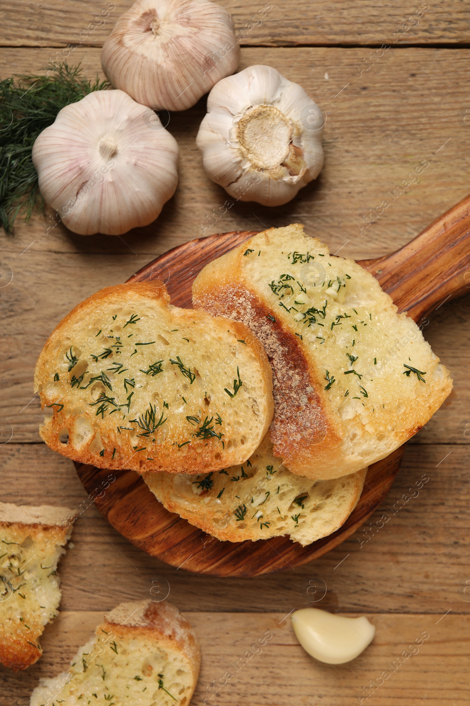 Photo of Tasty baguette with garlic and dill on wooden table, flat lay