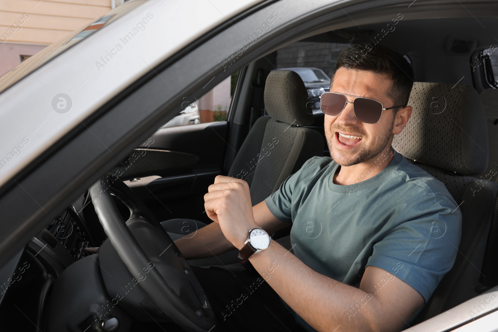 Photo of Listening to radio while driving. Handsome man with stylish sunglasses enjoying music in car