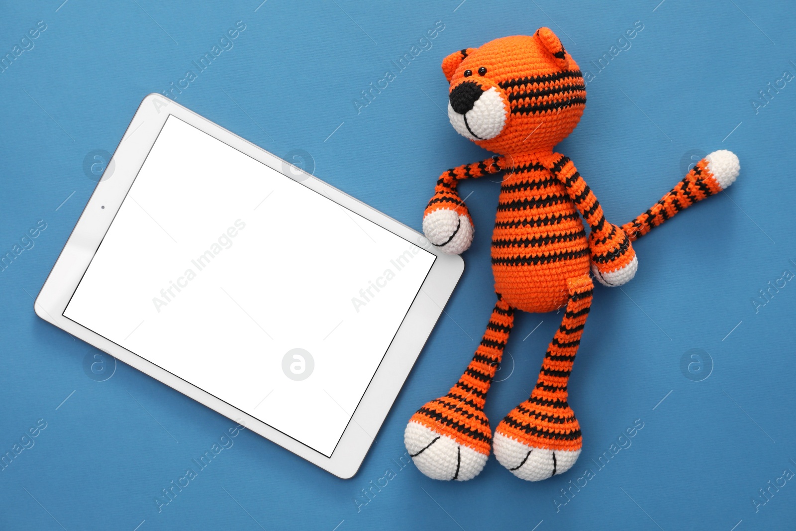 Photo of Modern tablet and toy tiger on blue background, flat lay. Space for text