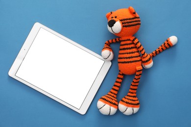 Photo of Modern tablet and toy tiger on blue background, flat lay. Space for text