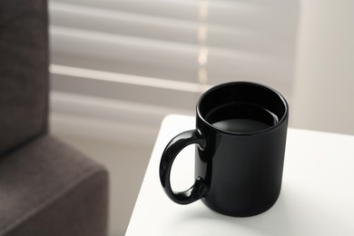 Photo of Black mug with drink on white table indoors. Mockup for design