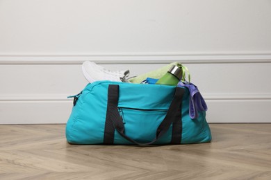 Photo of Blue gym bag with sports accessories on floor near white wall indoors