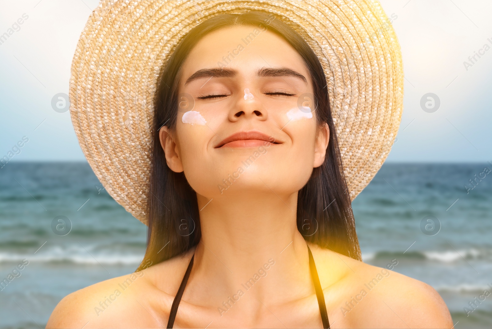 Image of Sun protection. Beautiful young woman with sunblock on her face near sea, closeup