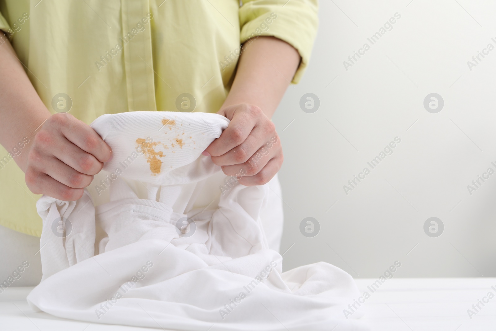 Photo of Woman holding shirt with stain at white table against light background, closeup. Space for text