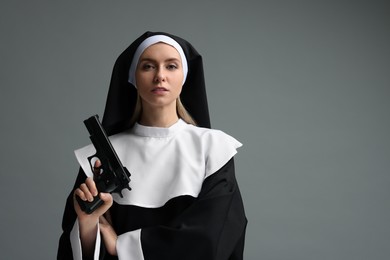 Woman in nun habit holding handgun on grey background. Space for text