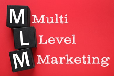 Image of Multi-level marketing. Abbreviation MLM of cubes with letters on red background, top view