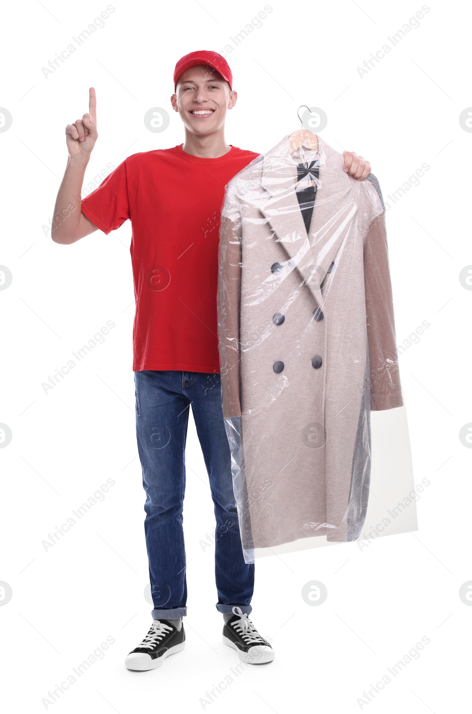 Photo of Dry-cleaning delivery. Happy courier holding coat in plastic bag and pointing at something on white background