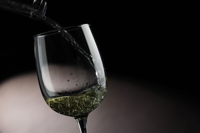 Photo of Pouring tasty aromatic wine in glass on dark background, closeup. Space for text
