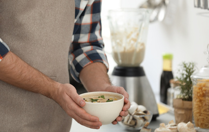 Photo of Young man holding bowl of tasty cream soup in kitchen, closeup