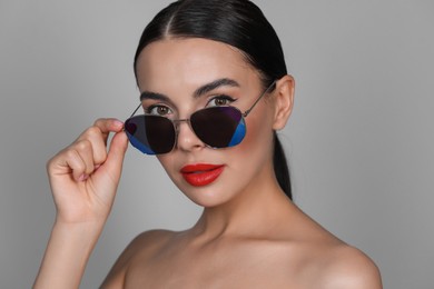 Photo of Attractive woman wearing fashionable sunglasses against grey background