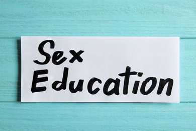 Photo of Piece of paper with phrase "SEX EDUCATION" on light blue wooden background, top view