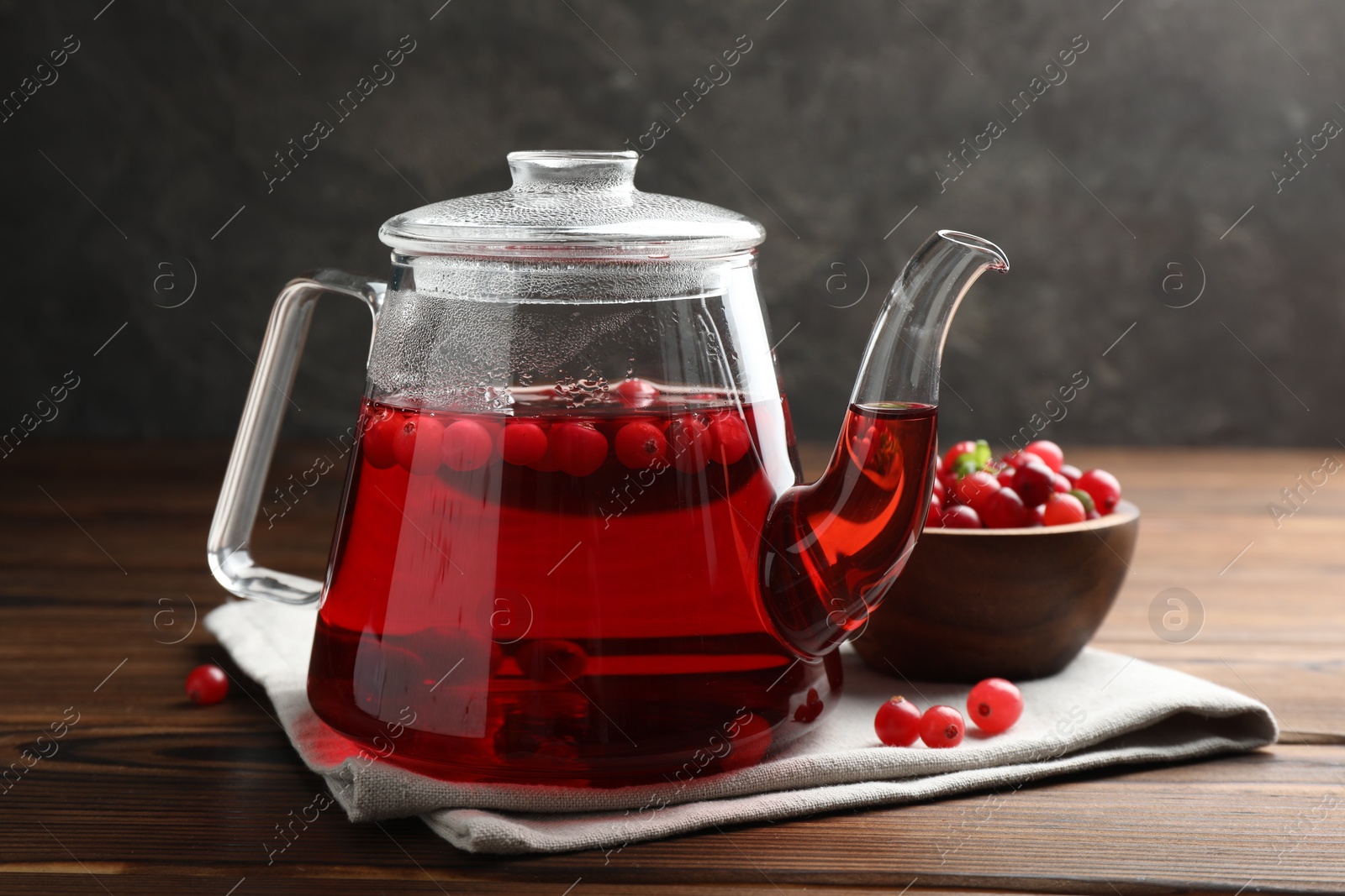 Photo of Tasty hot cranberry tea in teapot and fresh berries on wooden table