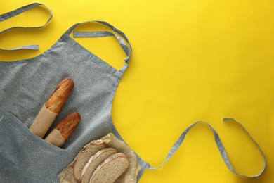 Photo of Clean kitchen apron with different types of bread on yellow background, flat lay. Space for text