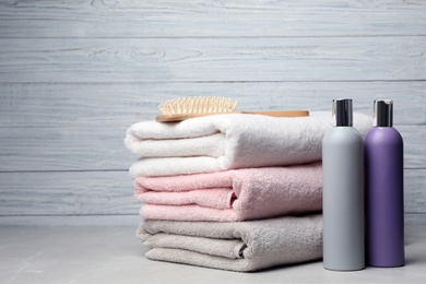 Photo of Towels with hair brush and shampoo bottles on table. Space for text