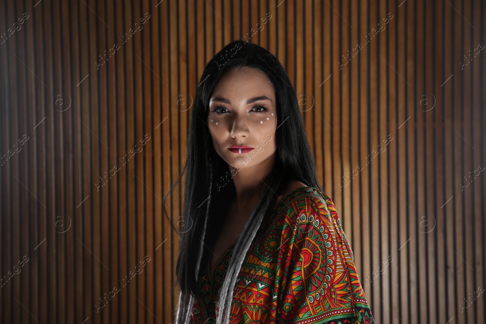 Photo of Portrait of young hippie woman with boho makeup in stylish outfit on wooden background