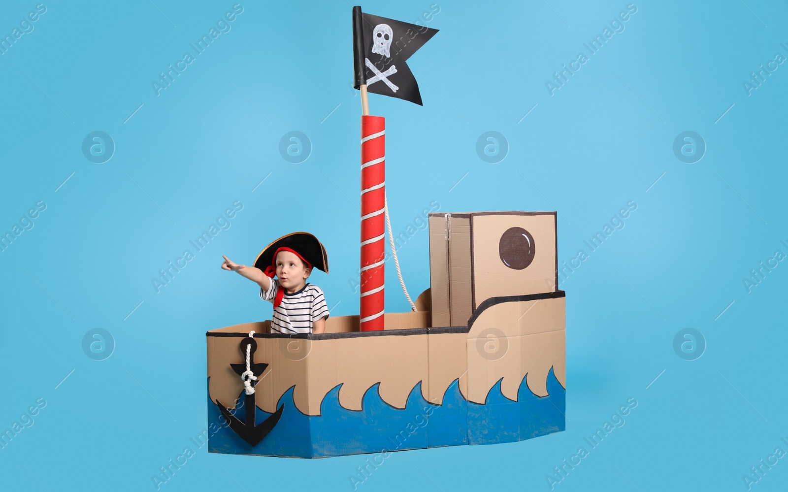 Photo of Cute little boy playing in pirate cardboard ship on turquoise background