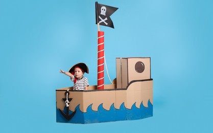 Photo of Cute little boy playing in pirate cardboard ship on turquoise background