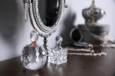 Photo of Small mirror, perfume bottles and jewelry on wooden table near light wall