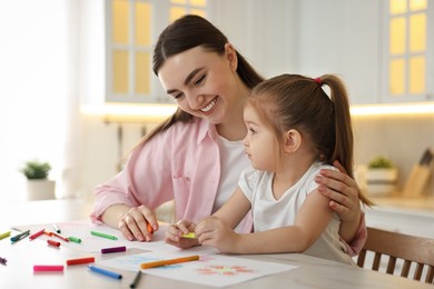 Mother and her little daughter drawing with colorful markers at table in kitchen