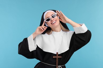 Happy woman in nun habit and sunglasses against light blue background