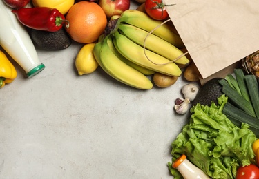 Photo of Paper bag with fresh vegetables and fruits on grey background, flat lay. Space for text