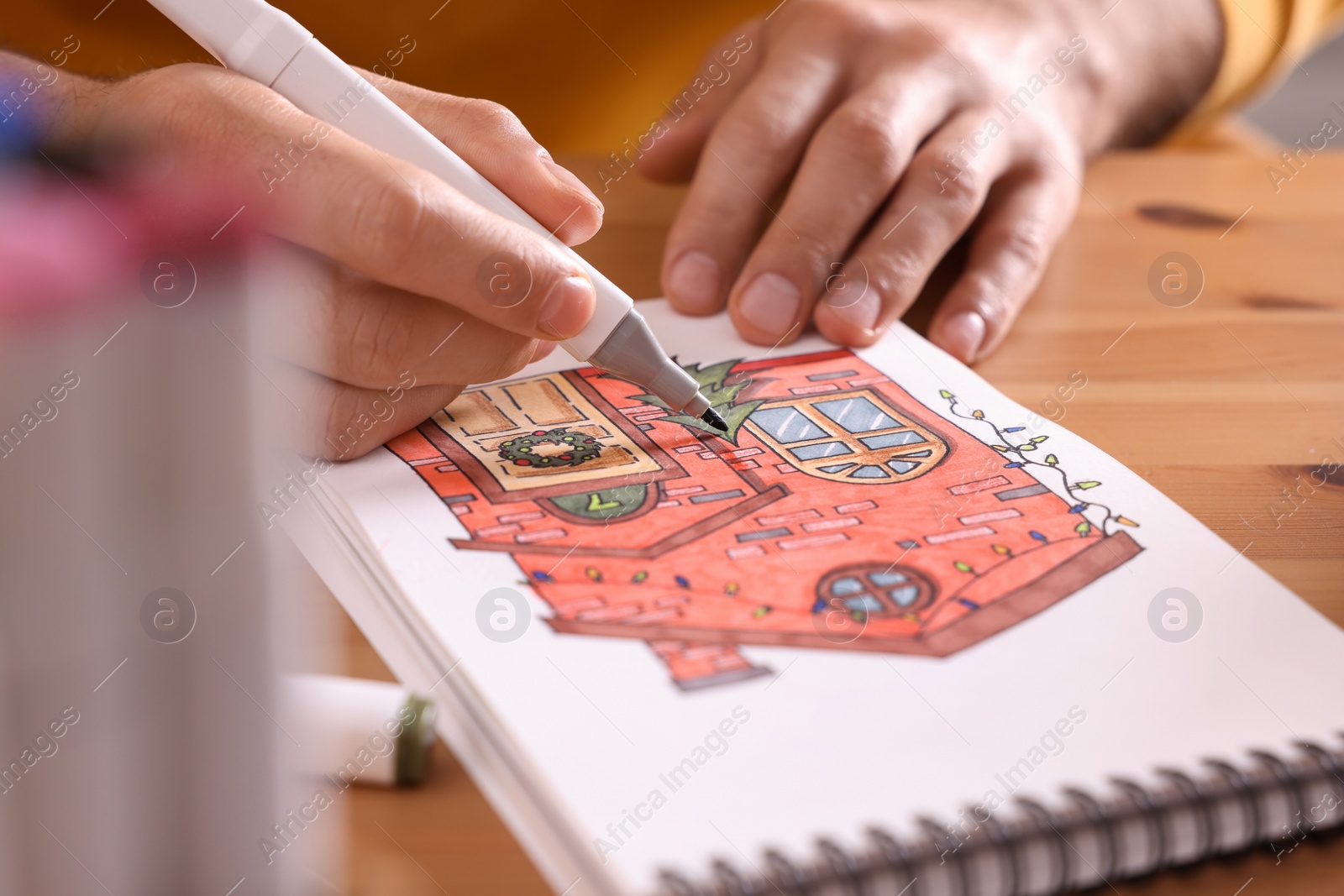 Photo of Man drawing in sketchbook with felt tip pen at wooden table, closeup