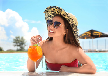 Photo of Woman with glass of refreshing drink in swimming pool