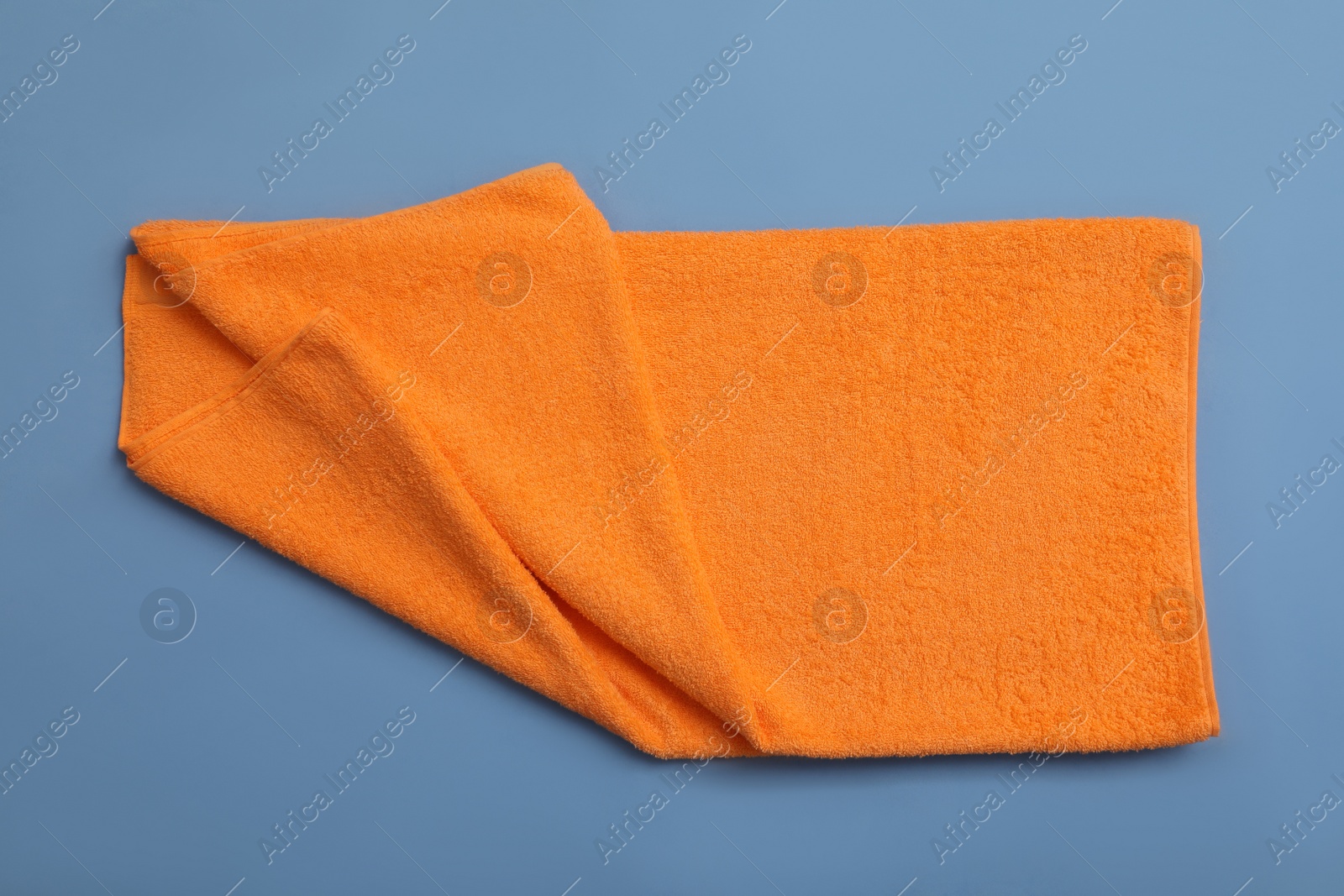Photo of Folded orange beach towel on blue background, top view
