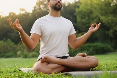 Photo of Man practicing yoga on mat outdoors, closeup. Lotus pose
