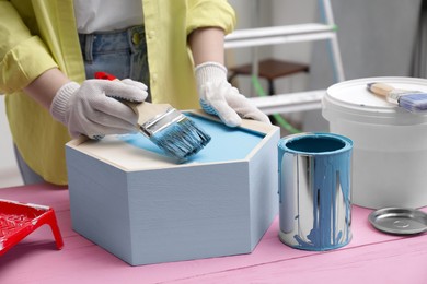 Woman painting honeycomb shaped shelf with brush at pink wooden table indoors, closeup