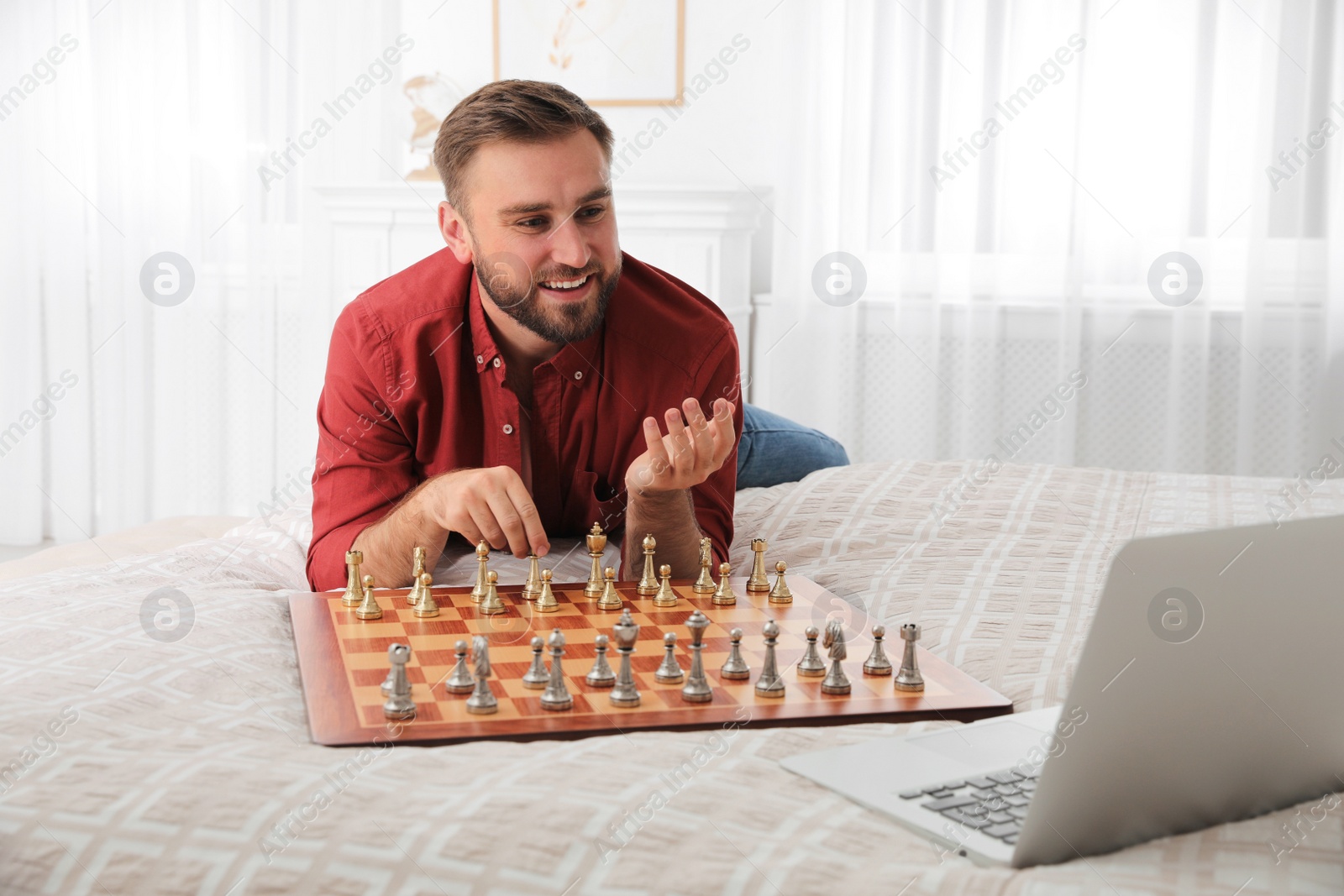 Photo of Young man playing chess with partner through online video chat on bed at home