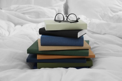 Hardcover books and glasses on white bed