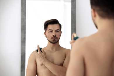 Photo of Handsome man using perfume in front of mirror