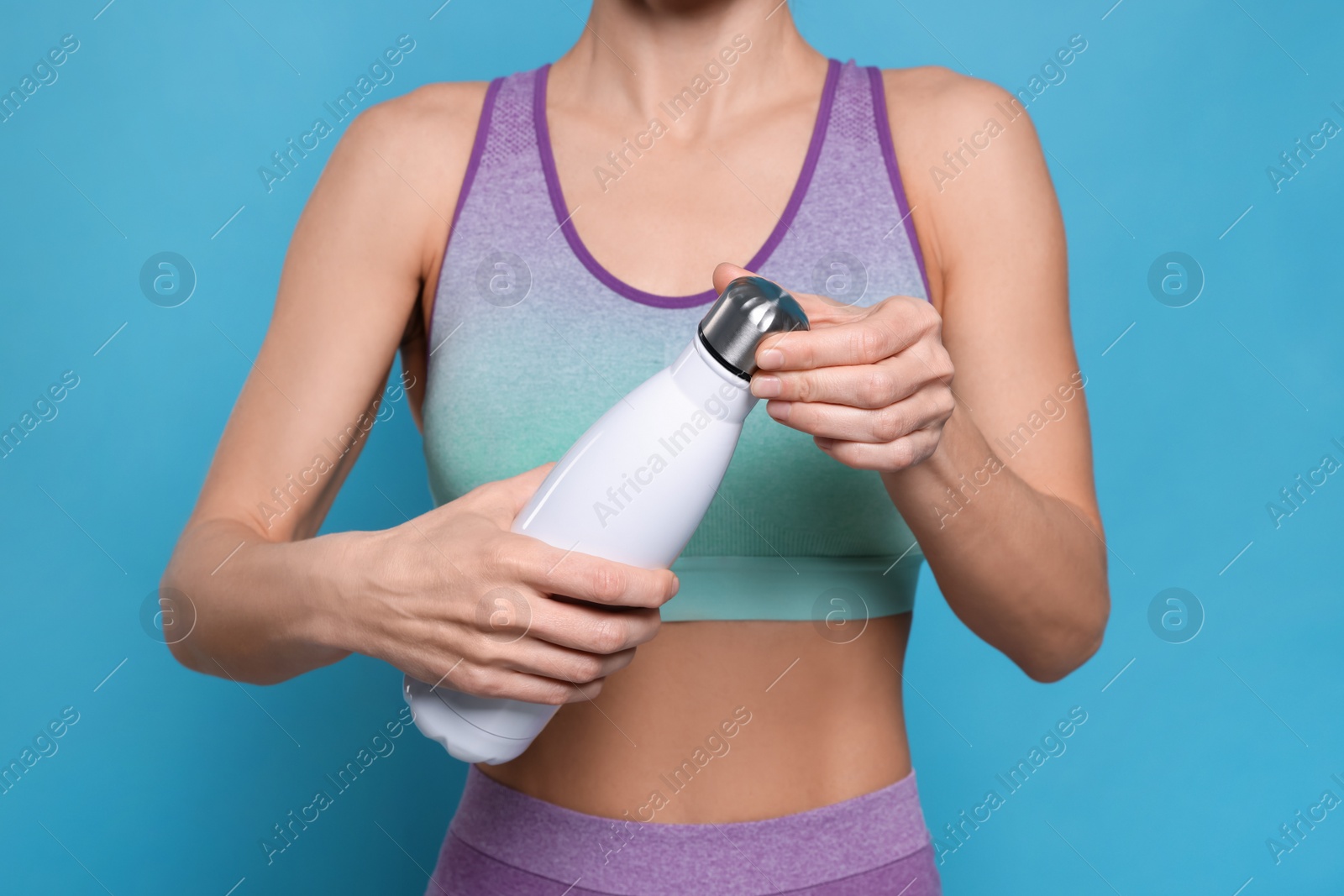 Photo of Sportswoman with thermo bottle on light blue background, closeup