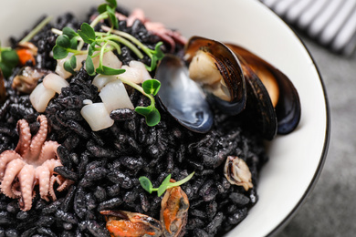 Delicious black risotto with seafood in bowl on table, closeup