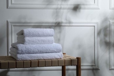 Photo of Stacked terry towels on wicker bench indoors, space for text