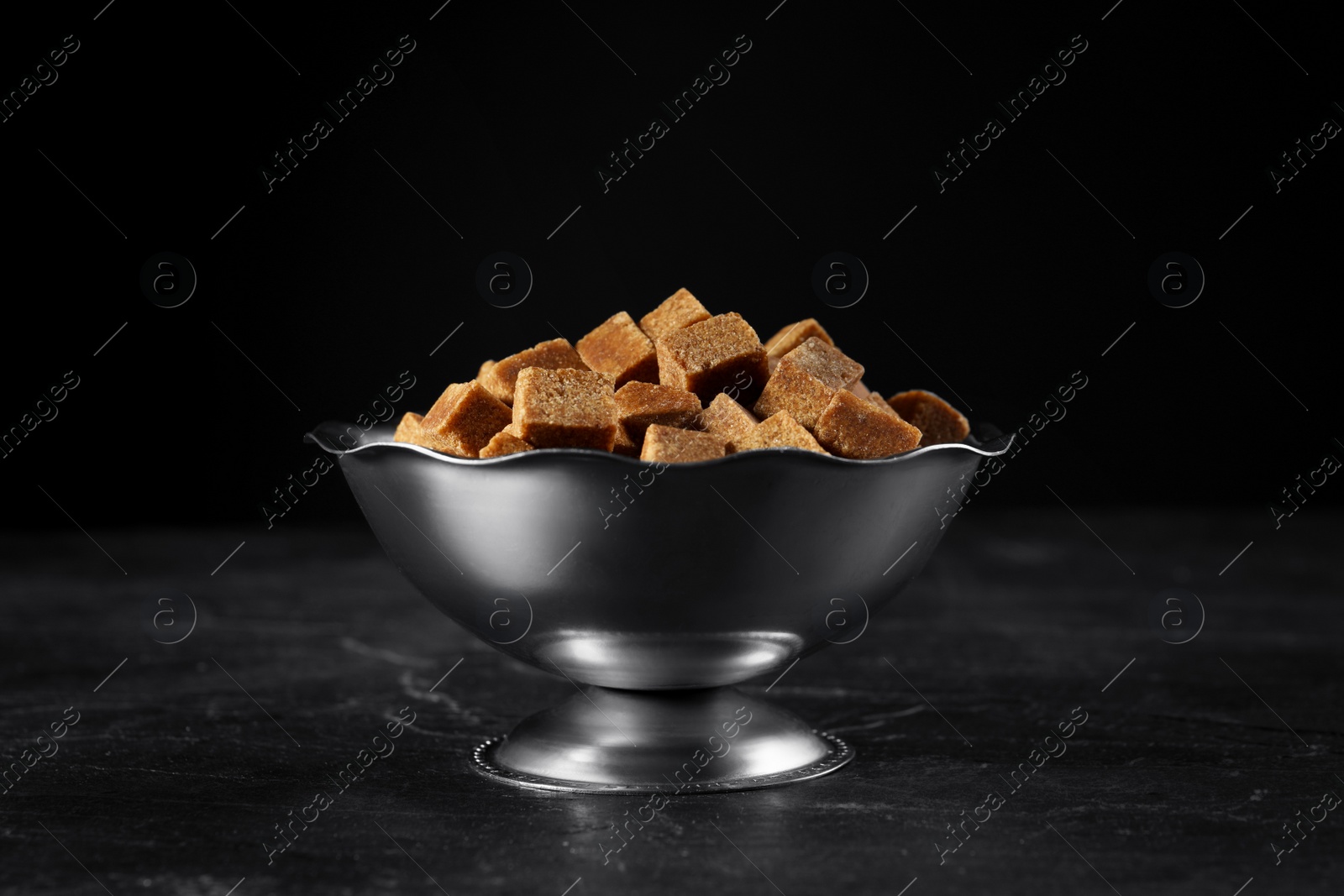 Photo of Metal bowl with brown sugar cubes on black table