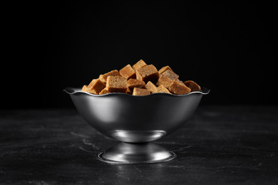 Photo of Metal bowl with brown sugar cubes on black table