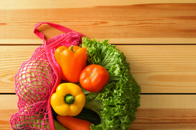 Photo of Net bag with vegetables on wooden table, top view