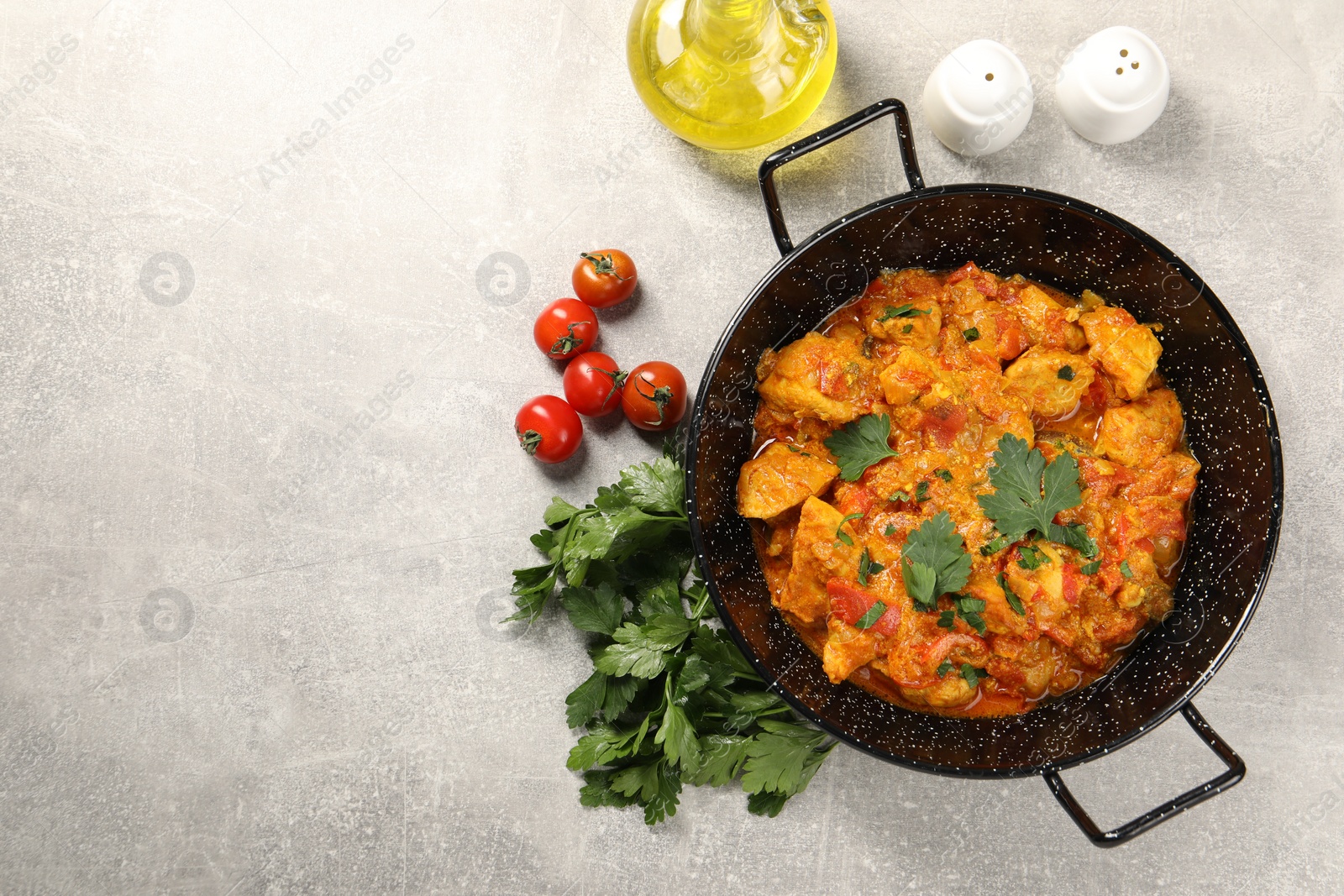 Photo of Delicious chicken curry in frying pan, parsley, tomatoes and oil on light grey table, flat lay. Space for text