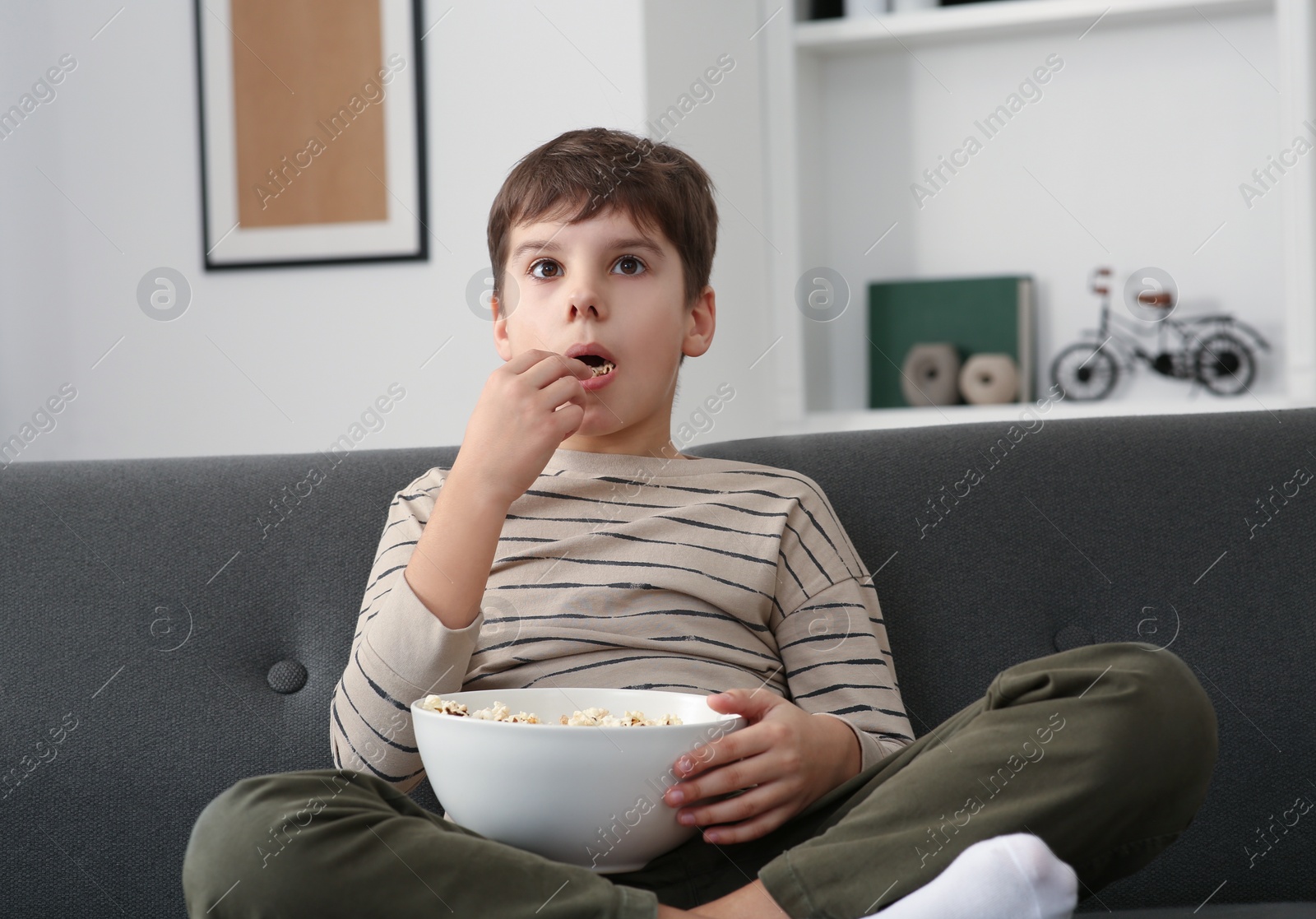 Photo of Little boy eating popcorn while watching TV at home