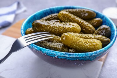 Photo of Fork with bowl of pickled cucumbers on light table, closeup