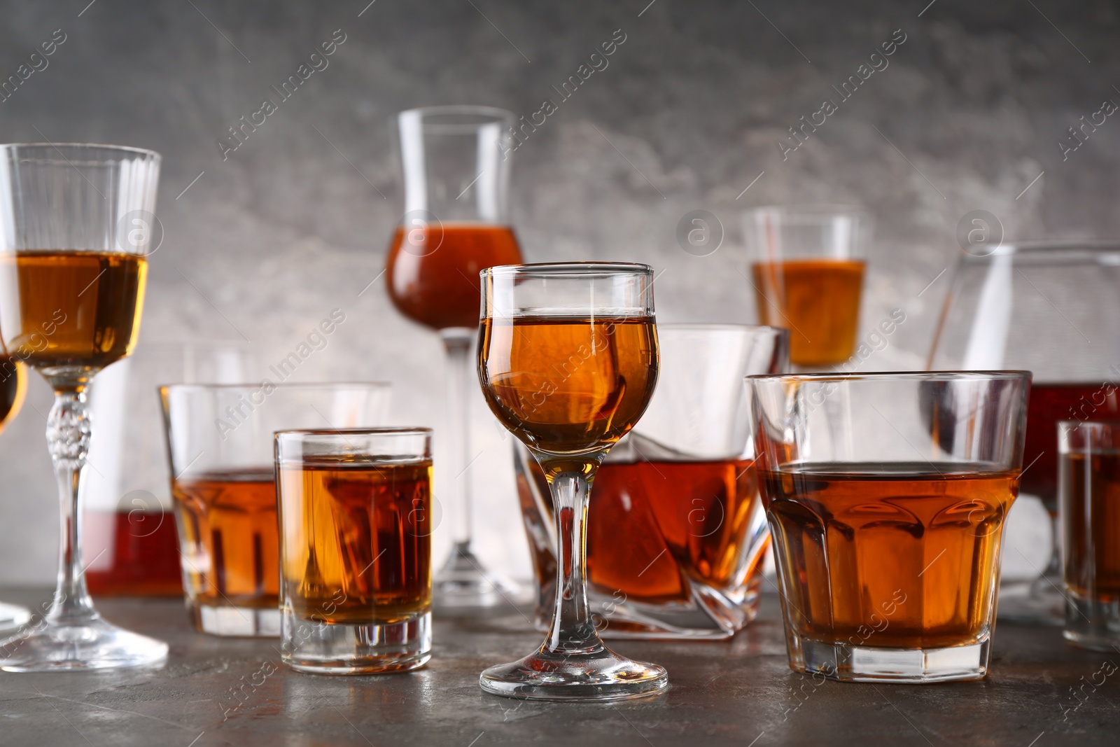 Photo of Different delicious liqueurs in glasses on grey table