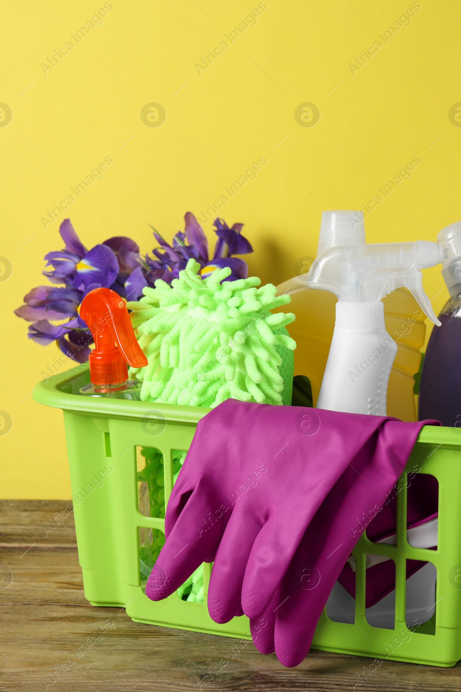 Photo of Spring cleaning. Basket with detergents, flowers and tools on wooden table