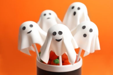 Photo of Delicious ghost shaped cake pops on orange background, closeup. Halloween celebration