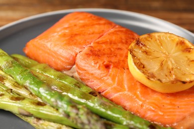 Photo of Tasty grilled salmon with asparagus and lemon on plate, closeup