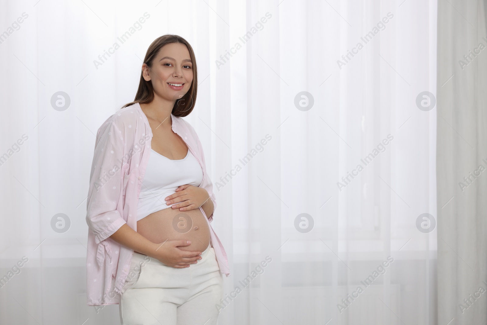 Photo of Beautiful pregnant woman near window indoors, space for text