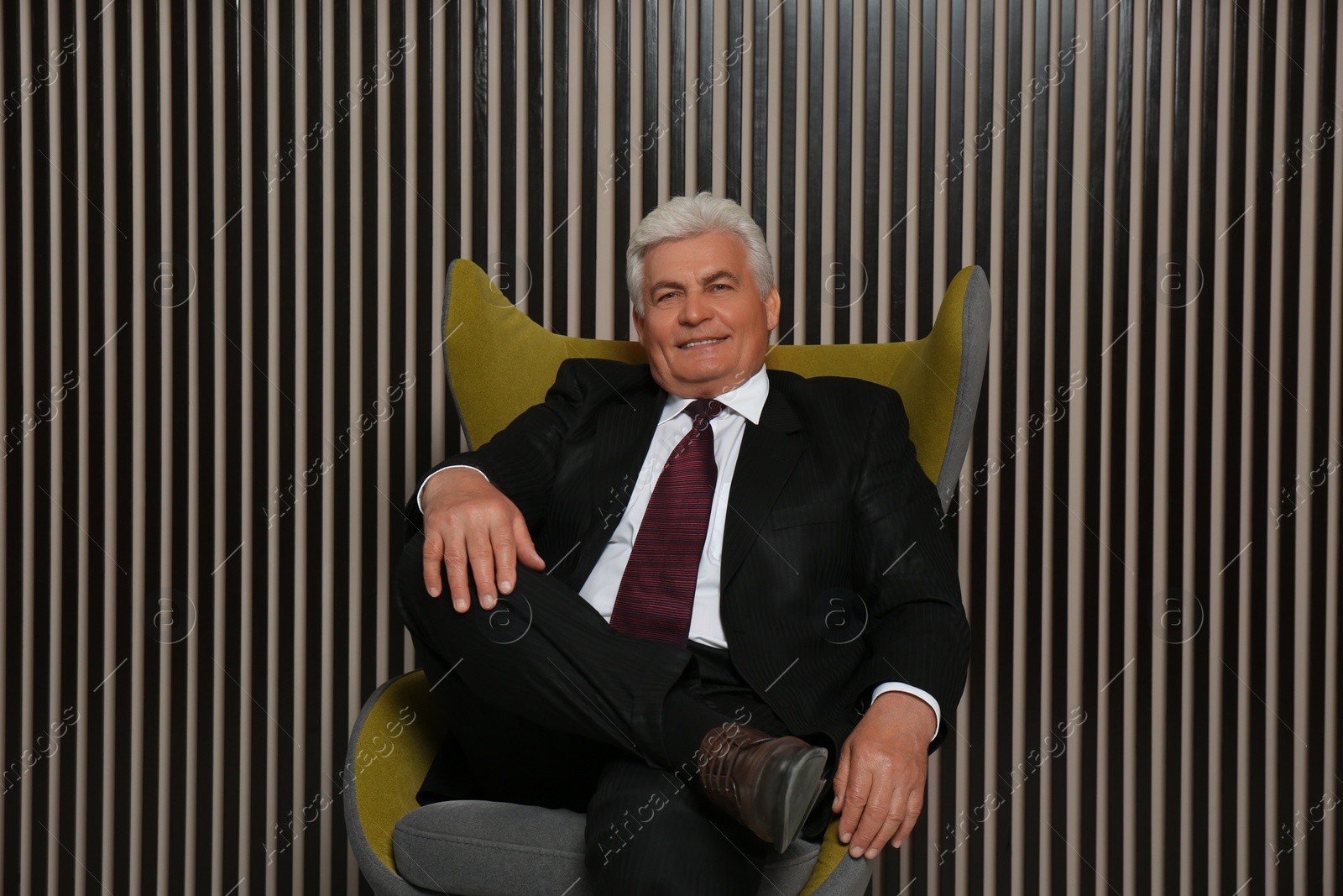 Photo of Happy mature businessman sitting in armchair near wood slat wall