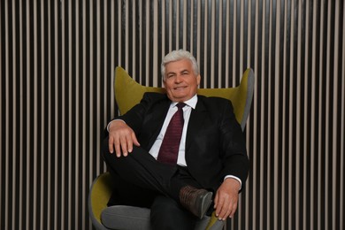 Photo of Happy mature businessman sitting in armchair near wood slat wall