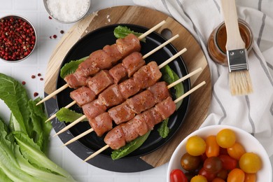 Photo of Wooden skewers with cut raw marinated meat on white tiled table, flat lay